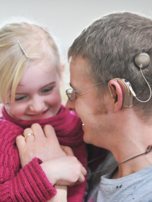 A man with a Cochlear Implant holding a little girl in his arms.